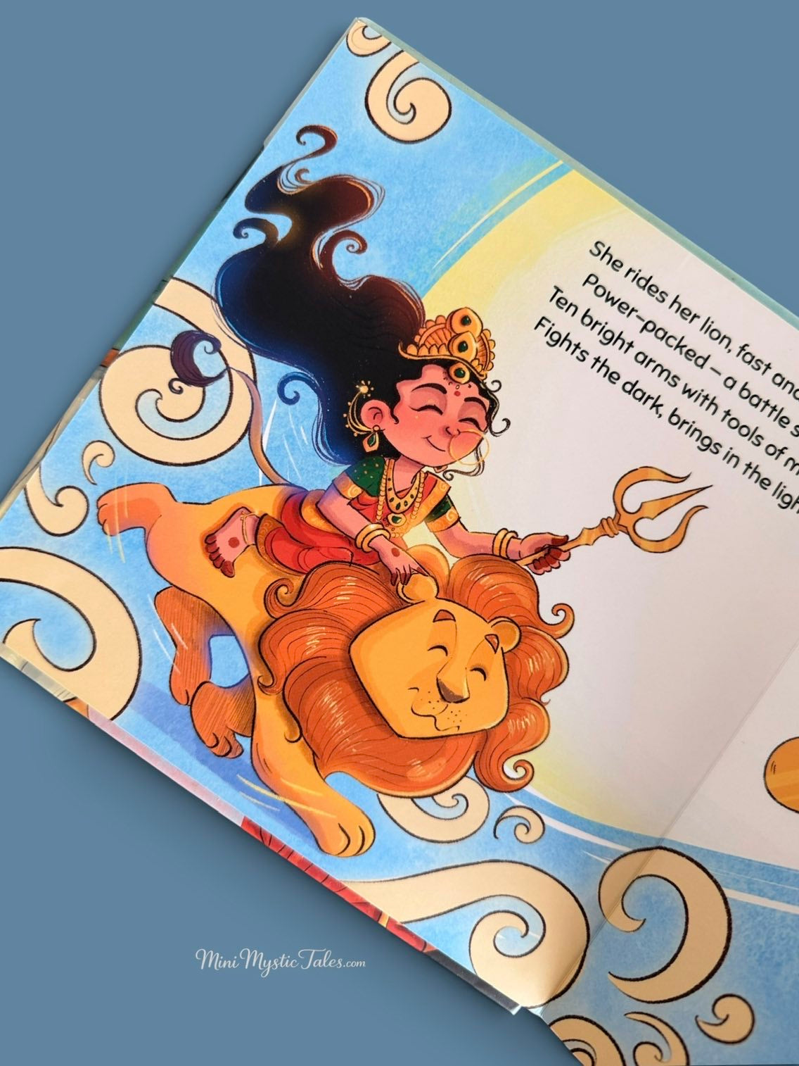 Colourful illustration of Durga Ma riding her lion with a trident from the children’s storybook Durga Ma The Lion Queen.