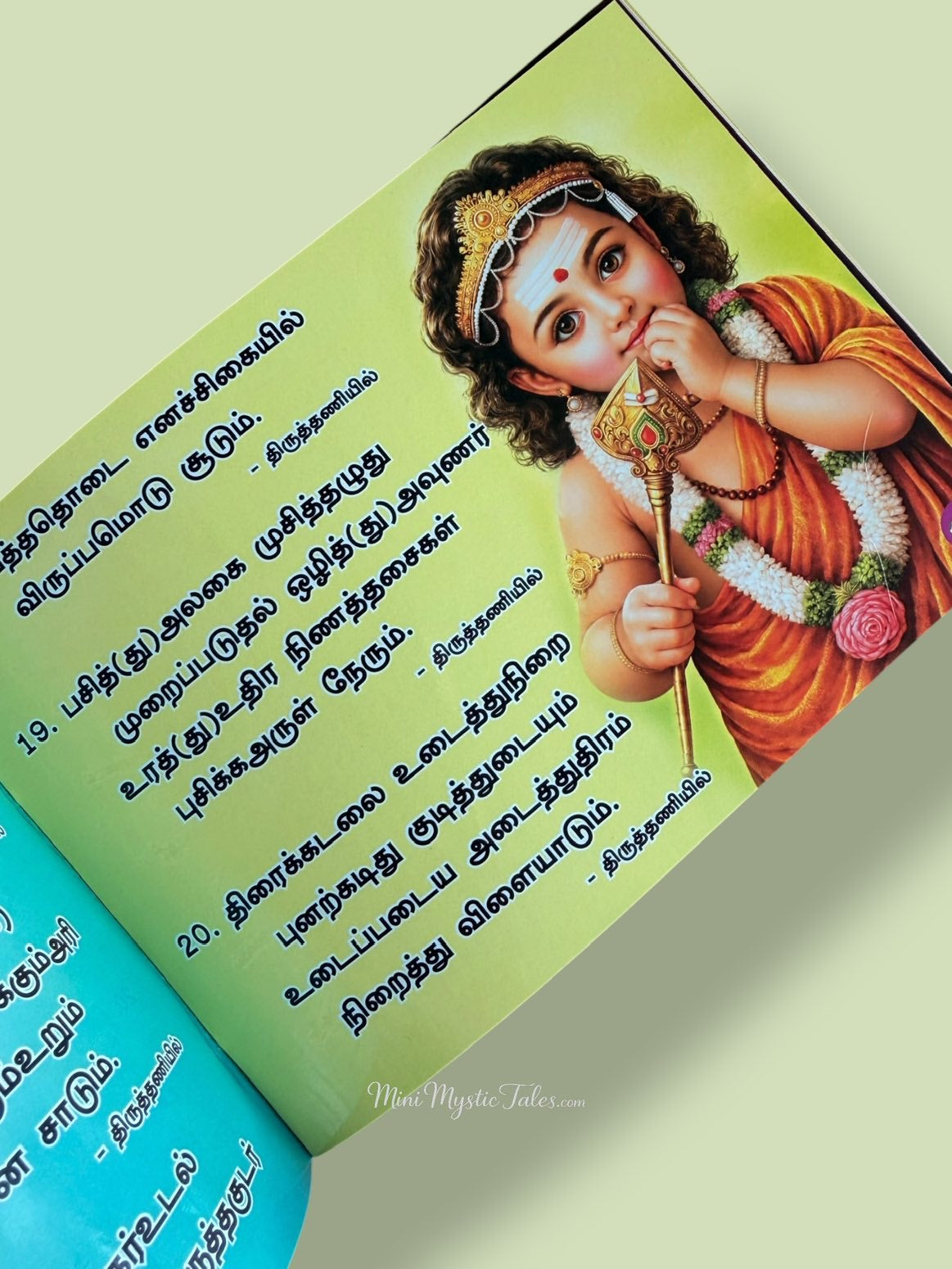 Beautiful illustration of child Lord Murugan holding the Vel in the Vel Maaral Tamil devotional book with sacred verses.